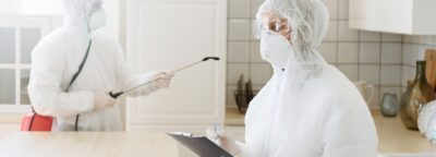 people with protective equipment are sanitized with a spray gun. Surface treatment due to coronavirus disease Covid-19. A man in a white suit disinfects a house. Virus pandemic