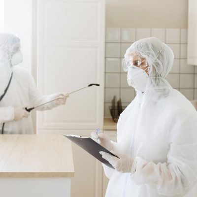 people with protective equipment are sanitized with a spray gun. Surface treatment due to coronavirus disease Covid-19. A man in a white suit disinfects a house. Virus pandemic